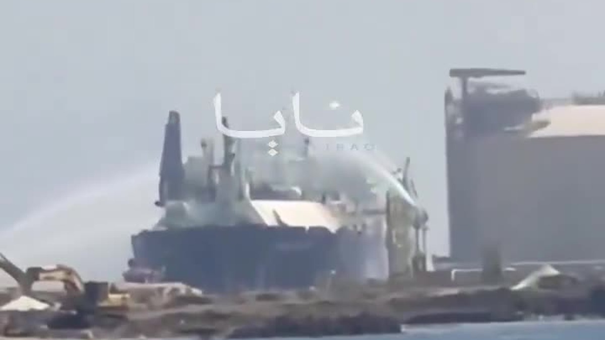 Navio de gás atracado no porto de Damietta recebe jatos de água de várias direções, com o tanque de estocagem do terminal ao fundo